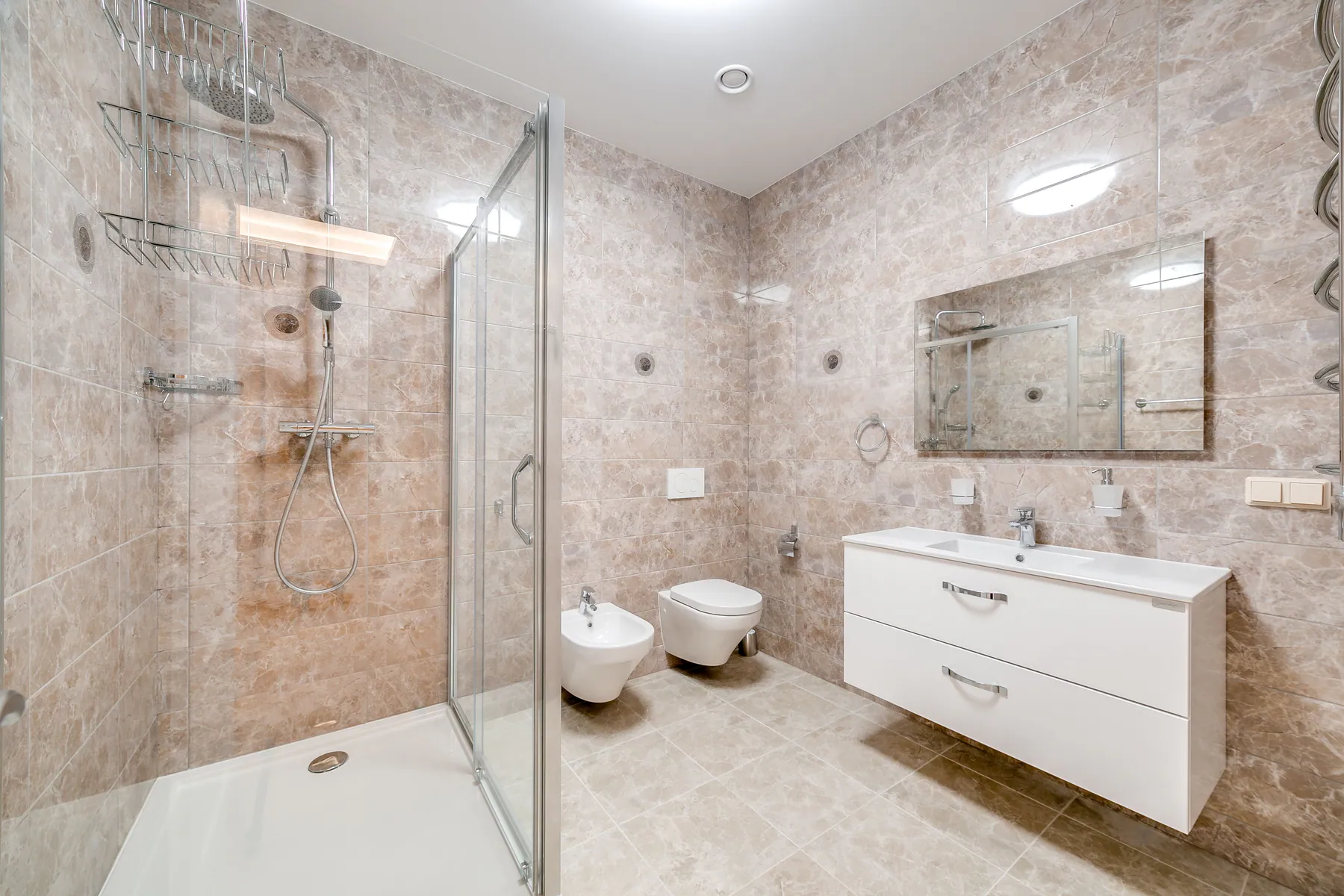Bright residential bathroom with clean shower, vanity, toilet, and tiled floor
