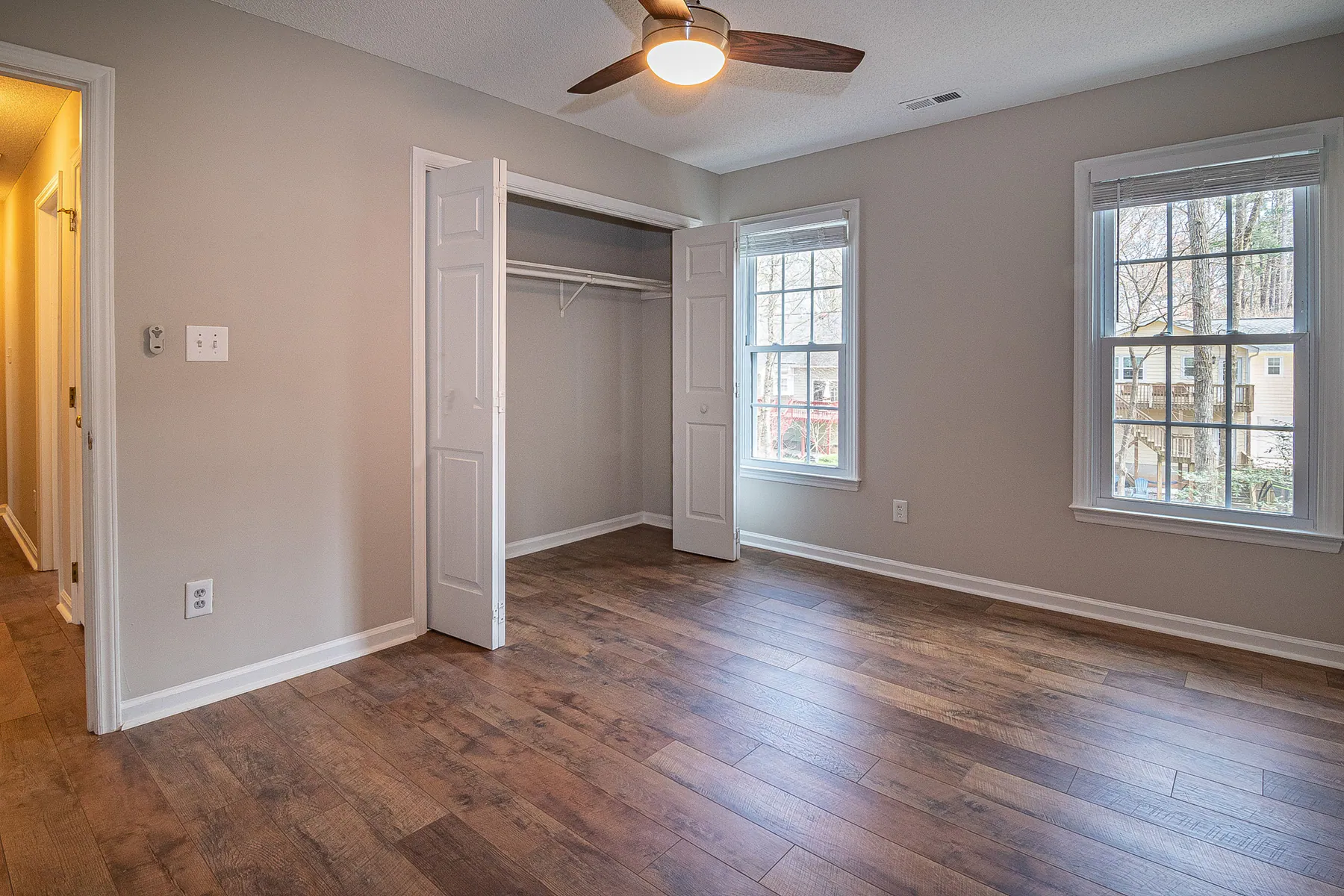 Empty bedroom with clean wood floor, open closet, and bright windows
