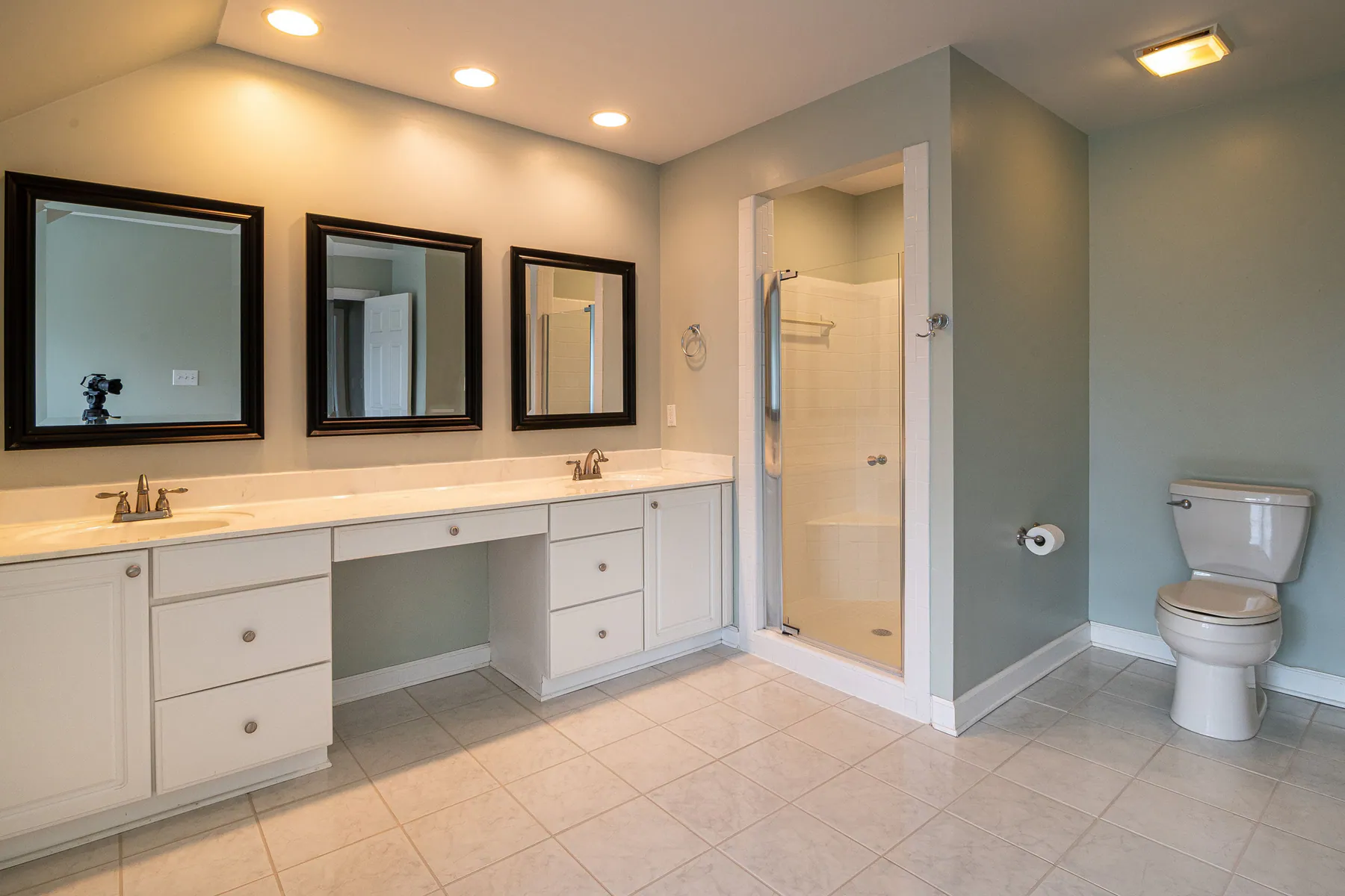 Large residential bathroom with clean vanity, shower, mirrors, and tiled floor