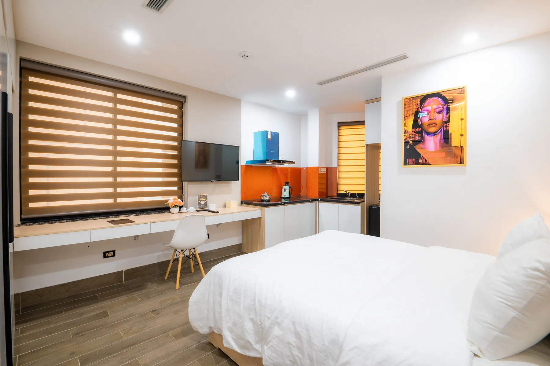 Modern short-term rental room with made bed, kitchenette, desk, and clear surfaces