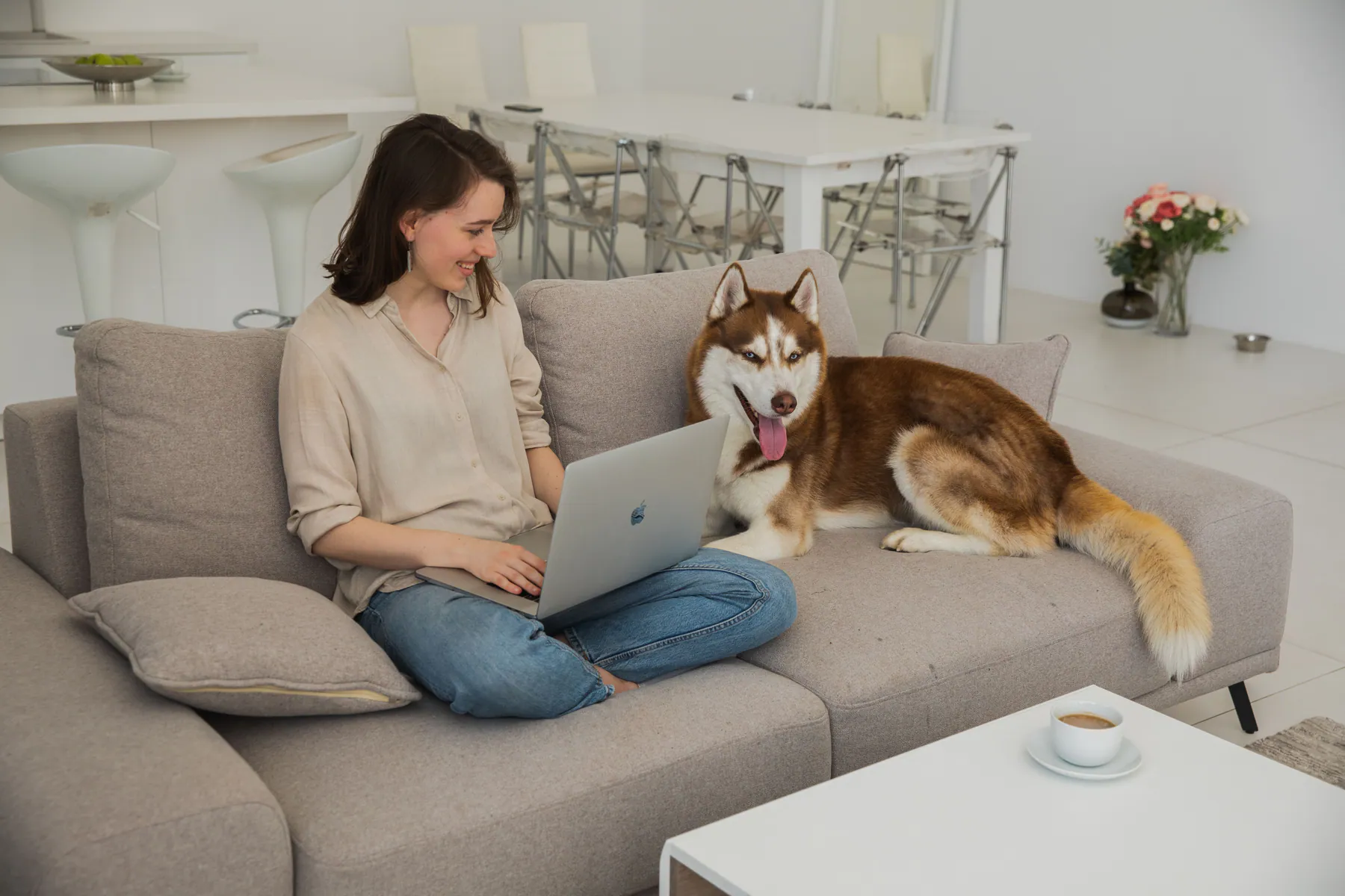 Woman working from a sofa beside her dog in a bright home